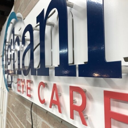 Ighani Eye Care sign seen almost edge-on, the navy and red letters standing well off the white face.