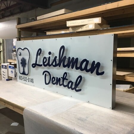 Leishman Dental panel sign on the bench in the shop, black script beside a tooth mark above the phone number.
