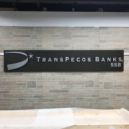 TransPecos Banks sign installed on stone, the brushed swoosh and star to the left of the name.
