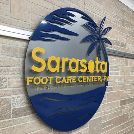 Sarasota Foot Care Center round sign with a navy palm and waves around yellow lettering, on stone.
