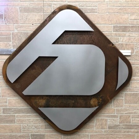 Diamond D Industries sign with a brushed steel monogram on a rusted diamond plate, mounted on stone.
