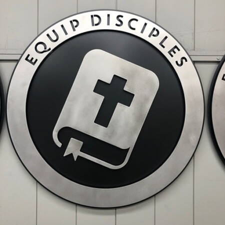 Northwood Baptist Church round sign reading Equip Disciples, an open book and cross in brushed steel.