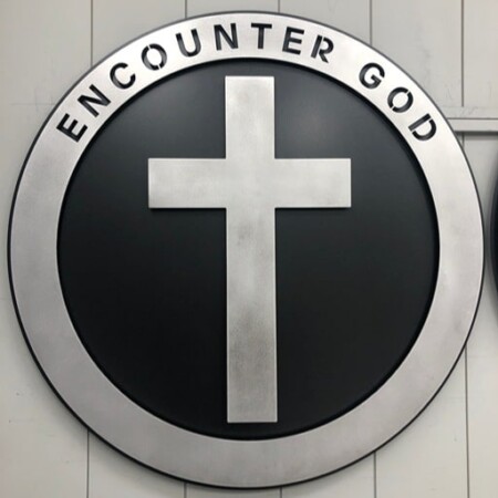 Northwood Baptist Church round sign reading Encounter God, a brushed steel cross on a black face.