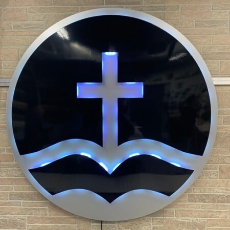 Living Word Church of Worcester round sign, a cross rising from brushed waves against a gloss black face.