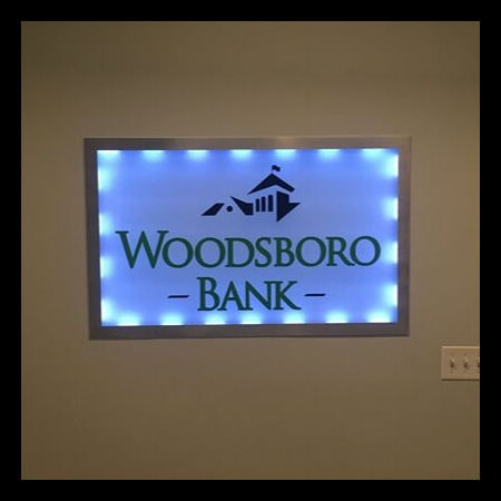 Woodsboro Bank edge-lit sign with a green barn mark above the name, lit white in the lobby.