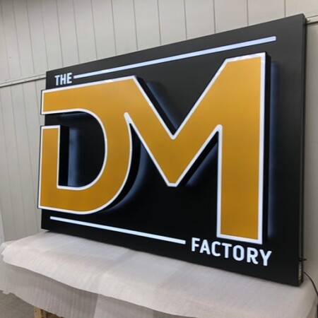 The DealMaker Factory face-lit led sign from the other side, the raised gold DM catching the shop lights.