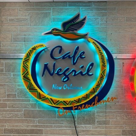 Halo-lit layered aluminum logo sign for Cafe Negril in navy/blue and yellow/orange/green patterned, glowing teal, mounted on a cleat.