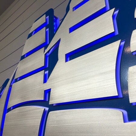 Halo-lit brushed aluminum dimensional-letter sign for Ariel Condominium in brushed silver and deep acrylic, glowing blue.