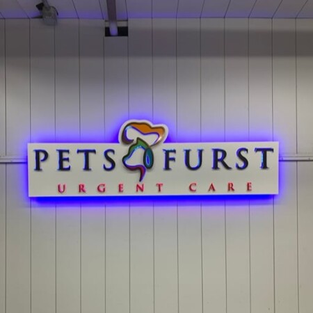 Pets Furst Urgent Care panel sign with a rainbow paw between the words, glowing blue behind the white face.