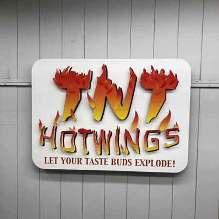 TNT Hot Wings sign with flaming letters over a white panel, Let Your Taste Buds Explode beneath.