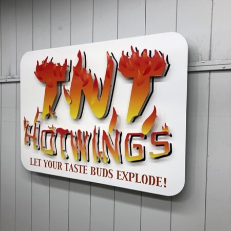 TNT Hot Wings sign angled on the wall, the flame tips standing off the panel edge.