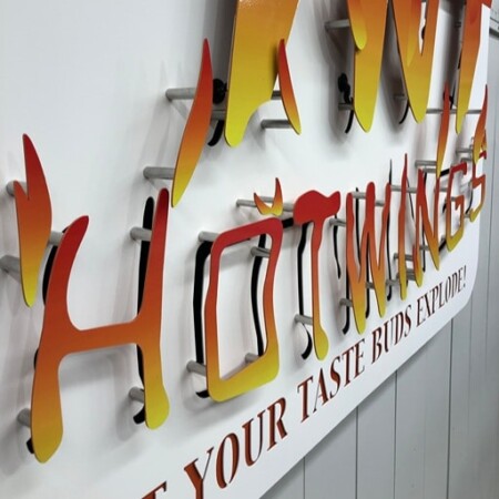Close view of the TNT Hot Wings letters on their standoffs, orange fading up into yellow.