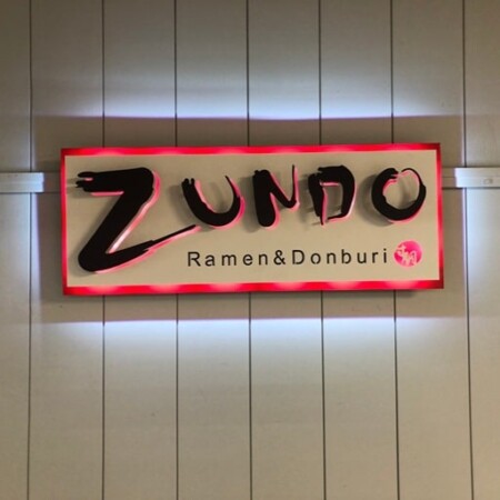 Zundo Ramen & Donburi sign, brushstroke lettering on a white panel with a red border, glowing red.