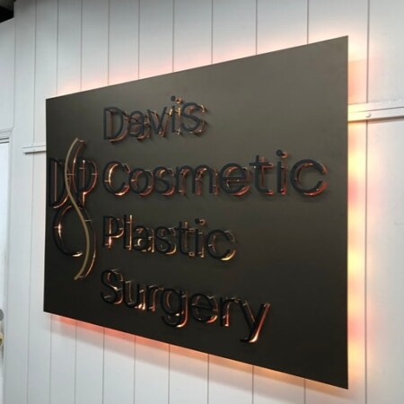 Davis Cosmetic Plastic Surgery panel sign in dark bronze with polished copper script, halo-lit LED and glowing warm white.