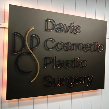 Davis Cosmetic Plastic Surgery panel sign in dark bronze with polished copper script, halo-lit LED and glowing warm white.
