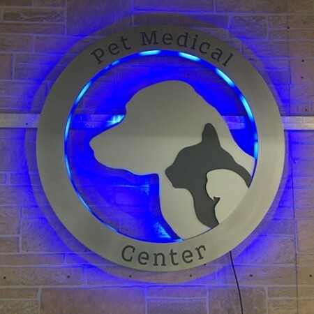 Pet Medical Center of Pasco round sign with a cat and dog cut inside a brushed ring, glowing blue.