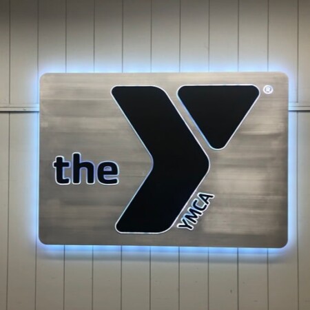 YMCA Frederick sign on a brushed panel, the black Y mark beside the word the, halo-lit and glowing white.