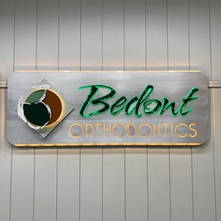Bedont Orthodontics halo-lit LED panel sign in brushed aluminum, green script over cut-out lettering, glowing warm white.