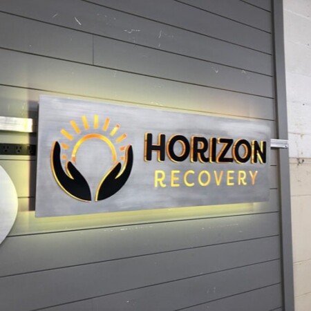 Horizon Recovery panel sign in brushed aluminum with a gold sunrise-in-hands mark, glowing warm.