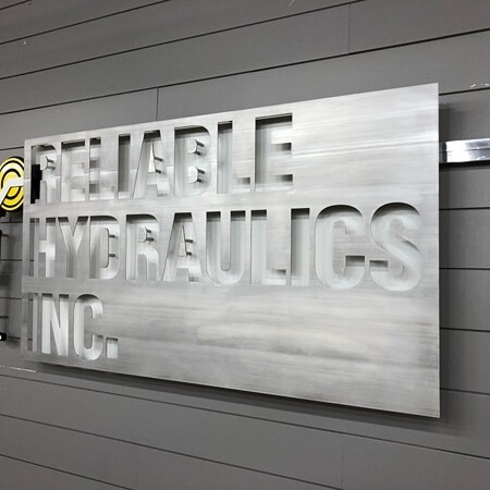 Reliable Hydraulics Inc. sign unlit, cutout letters on a brushed panel with almost no contrast.