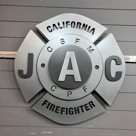 California JAC Firefighter badge unlit, the brushed steel layers reading as shadow and highlight.