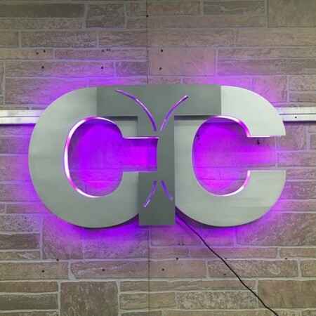 CTC monogram sign in brushed steel, the paired Cs halo-lit LED and glowing magenta on brick.