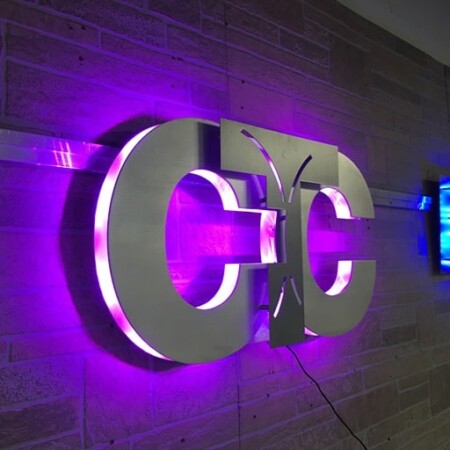 CTC monogram sign in brushed steel, the paired Cs halo-lit LED and glowing magenta on brick.