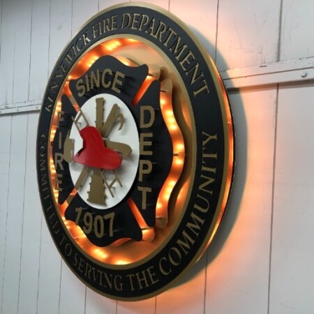 Kennewick Fire Department round badge, a red helmet over crossed tools, its amber LED ring glowing.