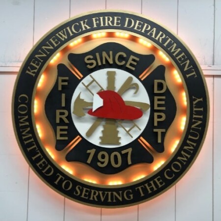 Kennewick Fire Department badge with the inner ring of LEDs lit warm behind the Maltese cross.