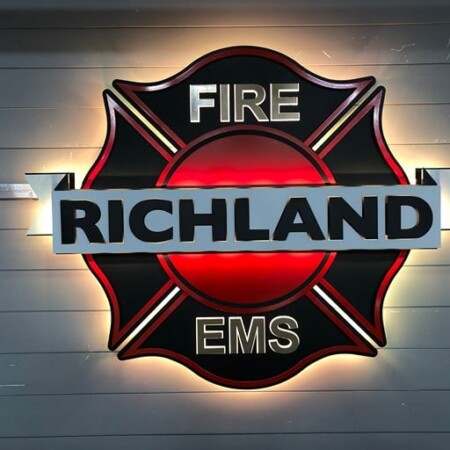 Richland Fire and EMS Maltese cross sign in red and black with a name bar across the center, glowing amber