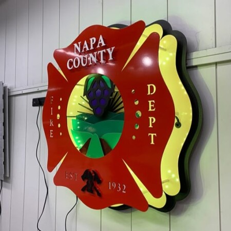 Angwin Volunteer Fire Department badge angled to show its layered depth, a yellow LED halo spilling onto the white wall.