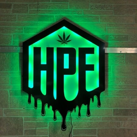 Hunny Pot Farms hexagon sign with HPF cut out beneath a cannabis leaf and a dripping lower edge, glowing green.
