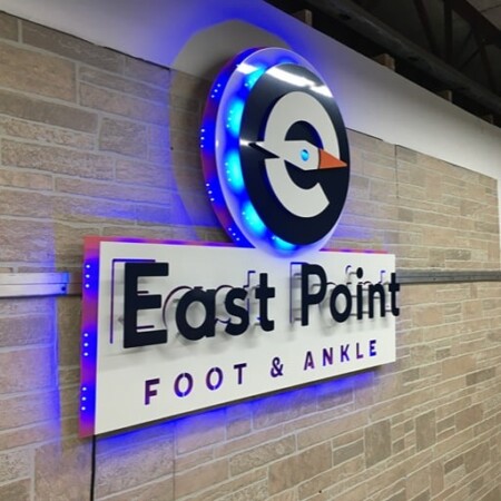 East Point Foot & Ankle round logo sign with a blue LED ring, above a white name panel on brick.