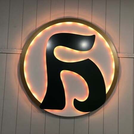 Hiwan Golf Club round sign with a black brand monogram, halo-lit LED and glowing warm amber.