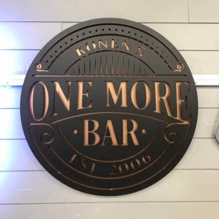 Konen's One More Bar round sign in dark bronze, the name and rules cut through a copper-toned face.