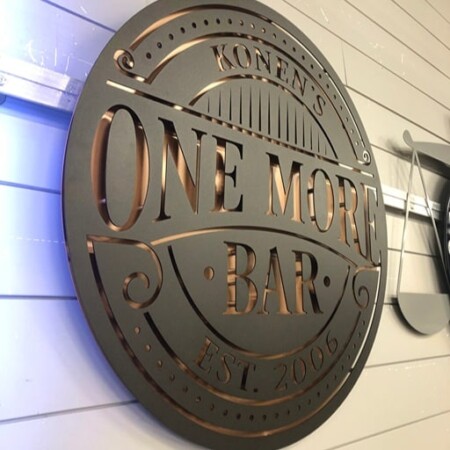Konen's One More Bar sign angled on the wall, blue light raking across the copper cut-outs.