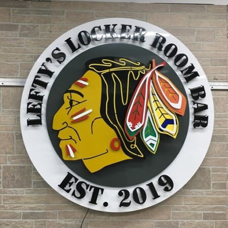 Lefty's Locker Room Bar sign in daylight, the layered gold and red logo inside raised rim lettering on brick.