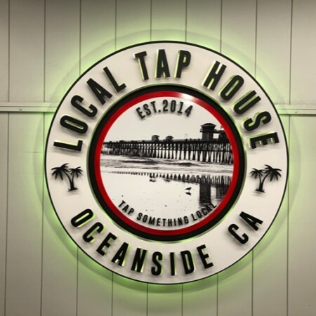 Local Tap House sign glowing green, the palm trees and rim lettering picked out by the halo.