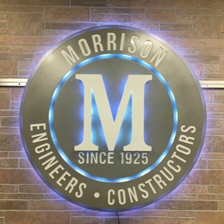 Morrison Engineers & Constructors sign lit, a blue and white LED halo picking out the ring and the gold M.