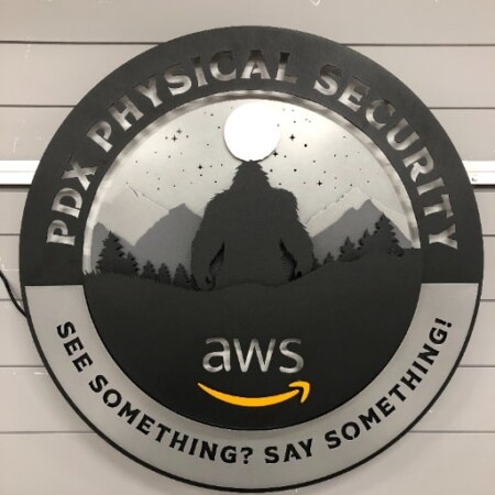 PDX Physical Security round sign with a bigfoot silhouette under the stars above the AWS mark, glowing blue.