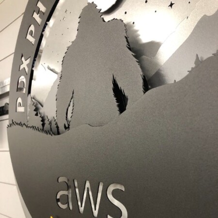 PDX Physical Security round sign with a bigfoot silhouette under the stars above the AWS mark, glowing blue.