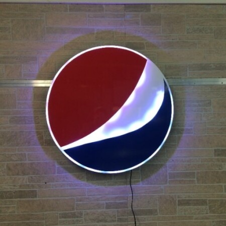 Pepsi globe sign in red, white and blue with the white band lit, mounted on stone.