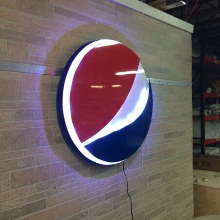 Pepsi globe sign angled on the wall, the lit white band curving across the gloss face.