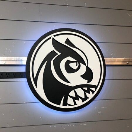 Rhystic Studies round sign with a black and white owl head, halo-lit LED and glowing blue.