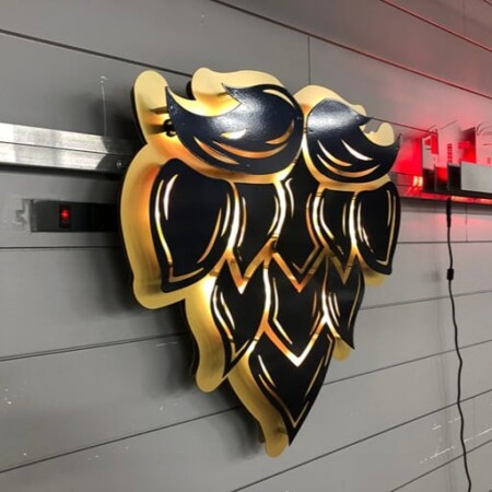 The Grand Barber beard sign from an angle, the gold underside catching the light between the layers.
