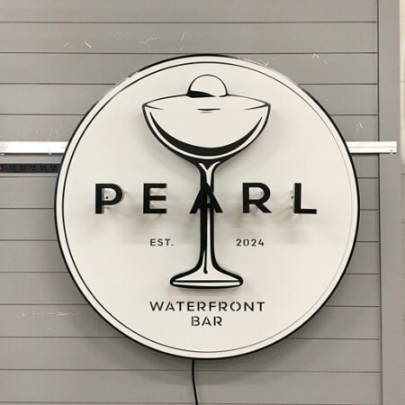Pearl Waterfront Bar round sign unlit, a cocktail glass drawn in line over a cream face.