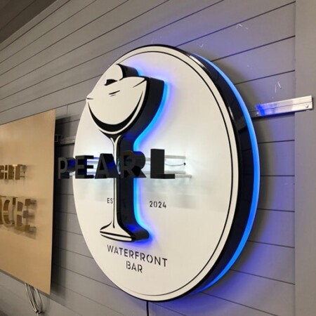 Pearl Waterfront Bar sign along the shop wall, the cocktail glass and Est. 2024 reading in raking light.