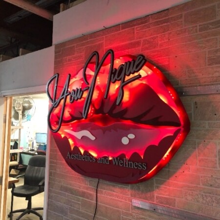 You Nique Aesthetics and Wellness sign shaped as red lips with script across them, glowing red on brick.