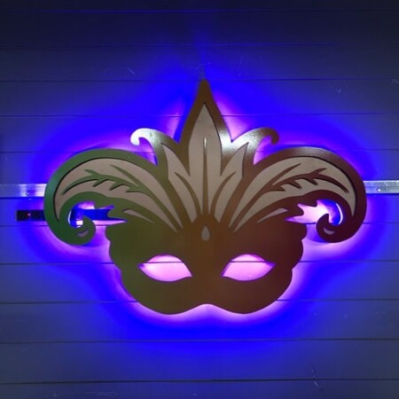 Boudreaux Cajun Steakhouse halo-lit LED Mardi Gras mask sign in a green-to-red gradient, glowing blue against a paneled wall.