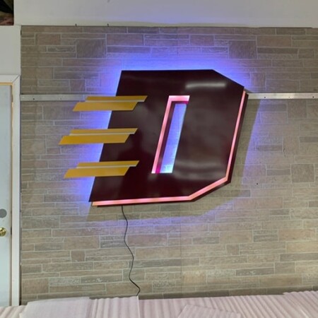 FID monogram sign in deep maroon with gold bars, halo-lit LED and glowing pink and blue.